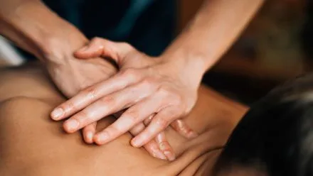 Close-up of a massage therapist's hands applying firm pressure to a bare upper back.